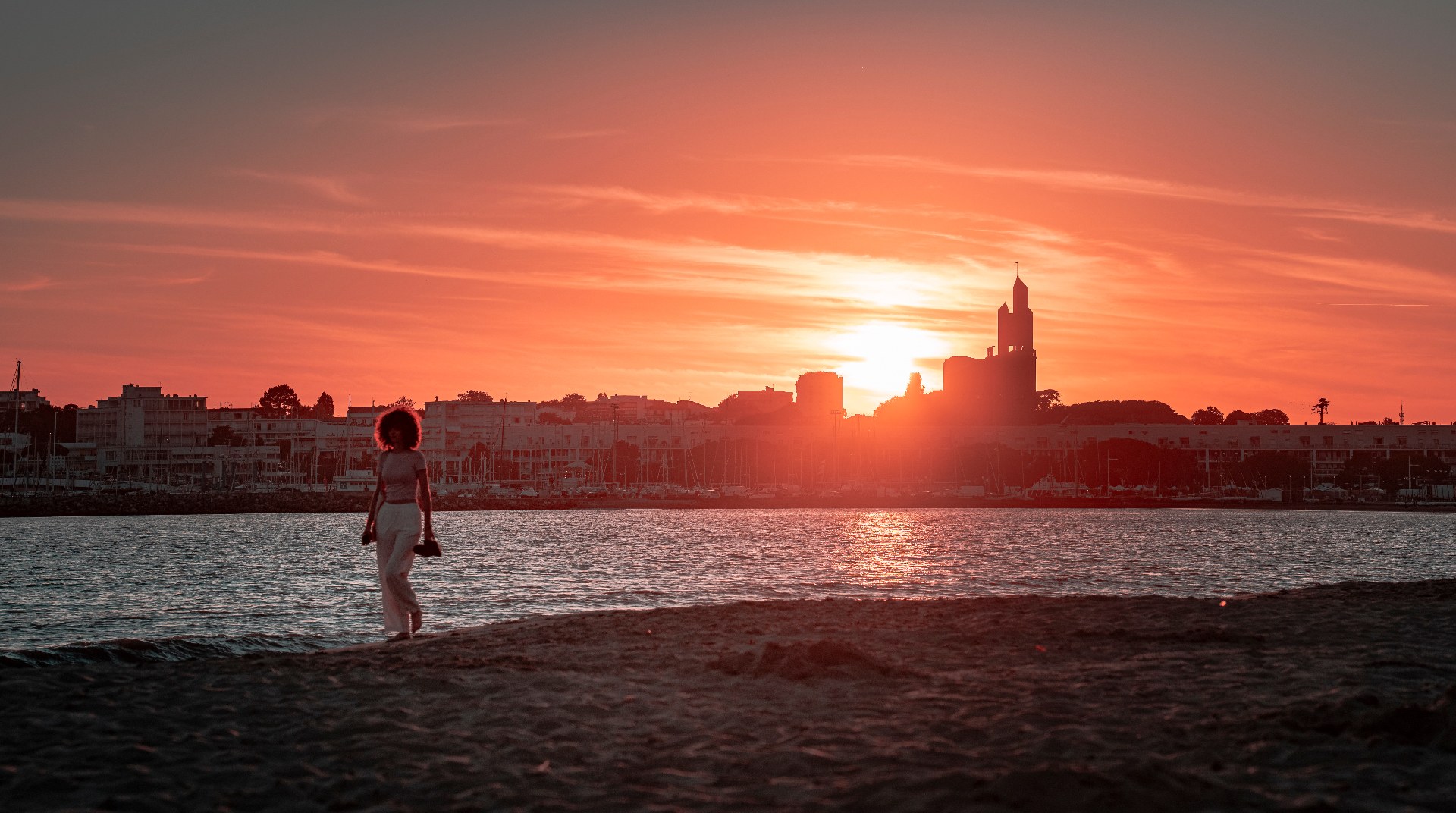 Coucher de soleil sur le port de Royan, silhouette d'une femme sur la plage et église Notre-Dame-des-Anges en arrière-plan