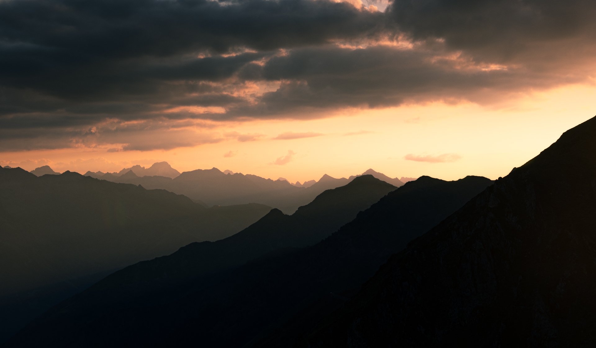 Couches de montagnes en dégradé sous un ciel orangé au coucher du soleil