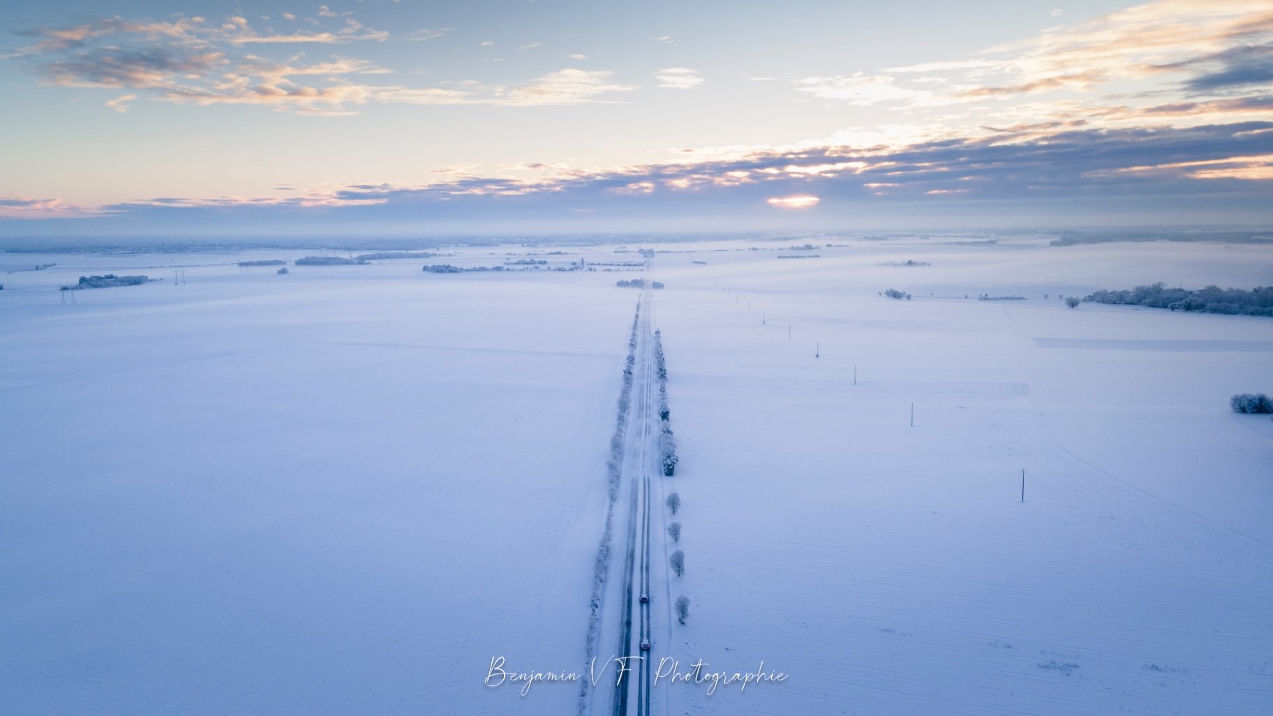 Route filante entre les champs enneigés au couchant, vue drone