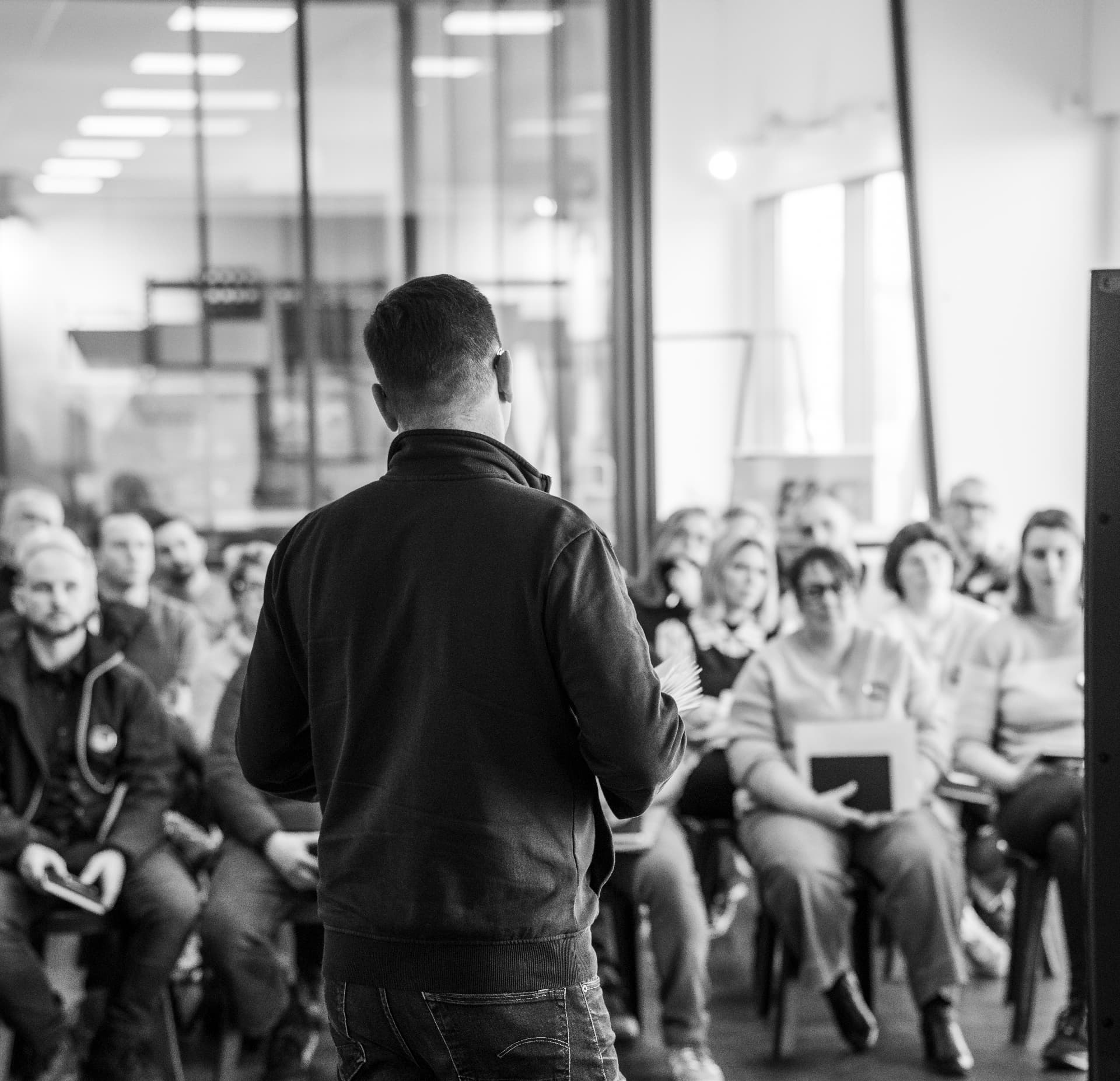 Orateur de dos s'adressant à une audience attentive lors d'une conférence, noir et blanc